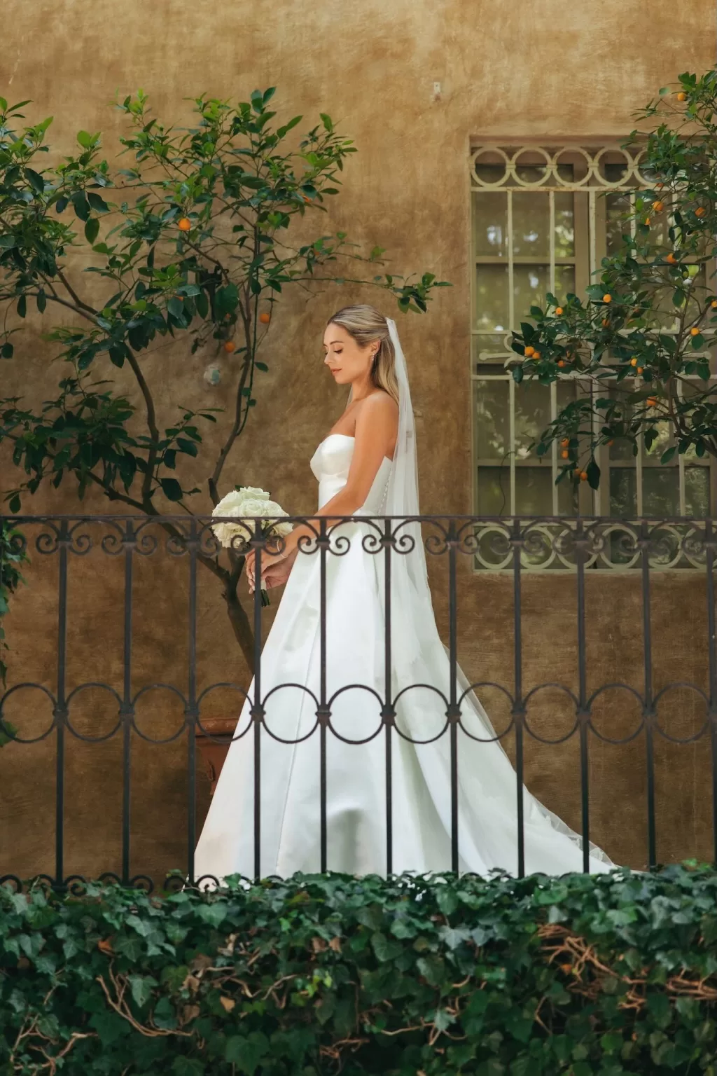 The bride walks gracefully through the citrus courtyard at Borgo Stomenanno, holding her bouquet.