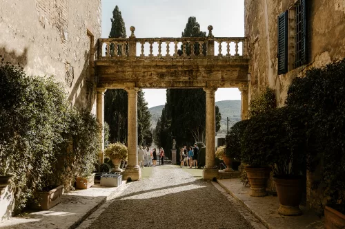 Guests mingling beneath stone archway framed by cypress trees at Borgo Stomennano.