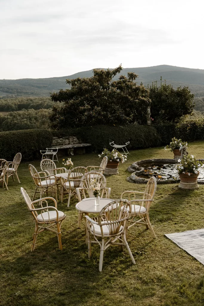 Outdoor lounge setup on manicured lawn at Borgo Stomennano, surrounded by topiary hedges and lemon trees with Tuscan hills in the distance.