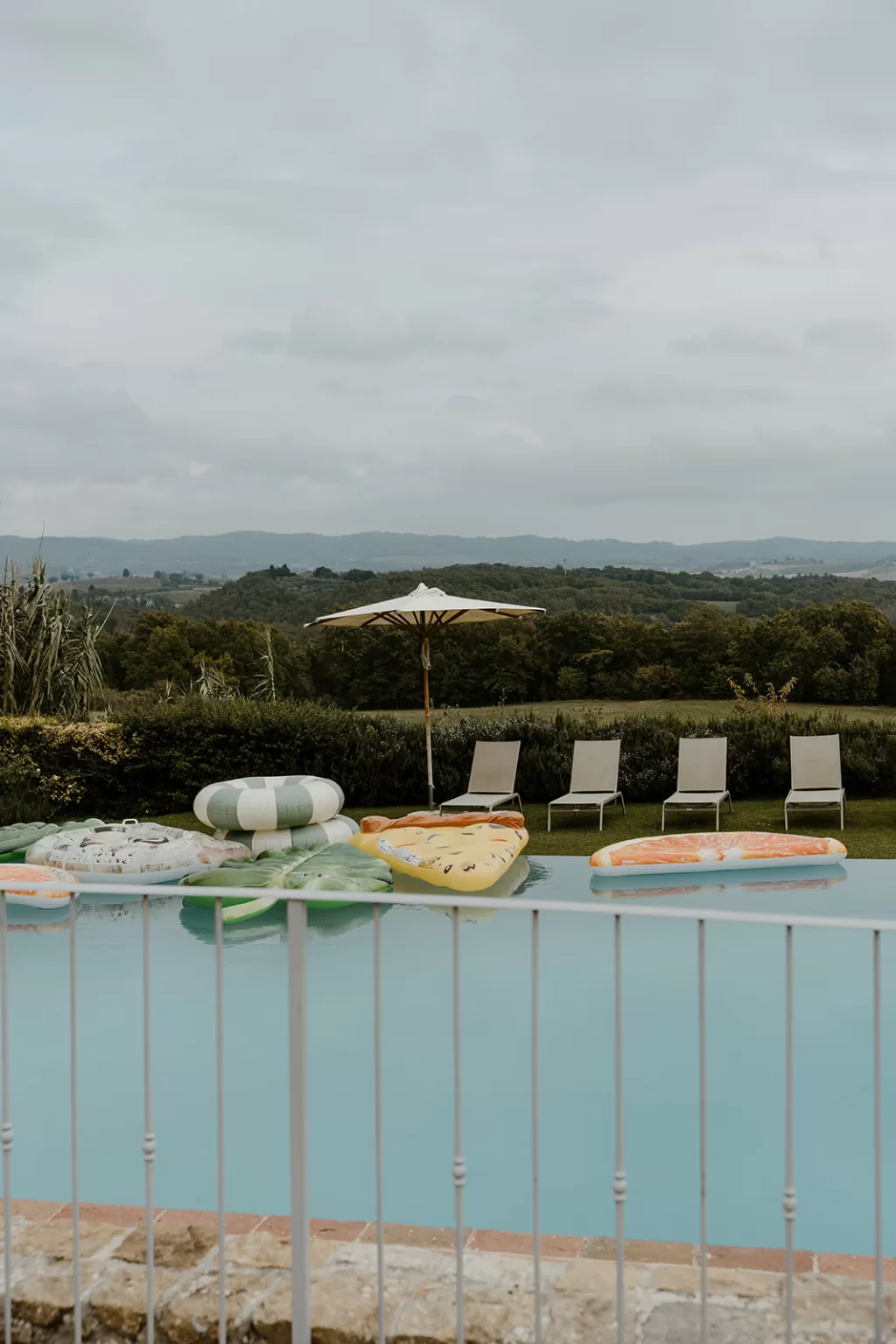 Serene poolside at Borgo Stomennano lined with sun loungers and shaded by umbrellas, overlooking green hills.