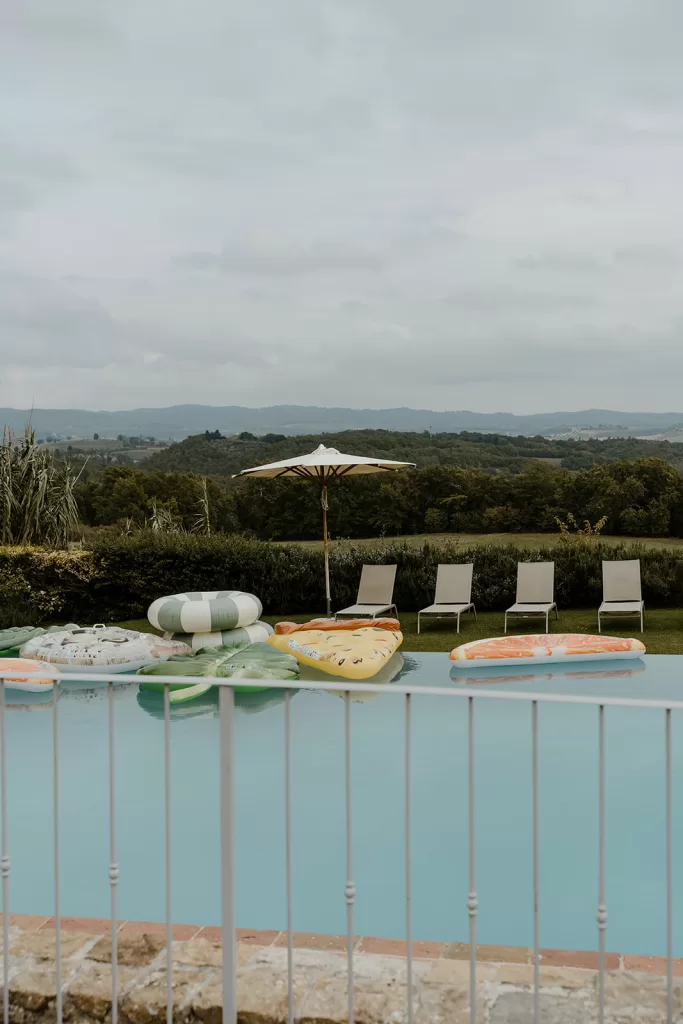 Serene poolside at Borgo Stomennano lined with sun loungers and shaded by umbrellas, overlooking green hills.