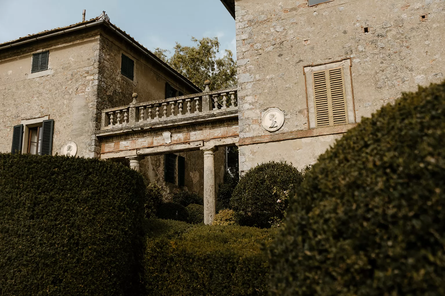 Stone balustrade and detailed architecture of the villa at Borgo Stomennano framed by sculpted hedges.