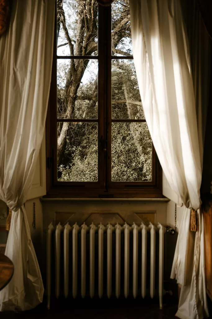 Soft curtains framing a tall window with a view of trees outside at Borgo Stomennano, capturing a peaceful moment indoors.
