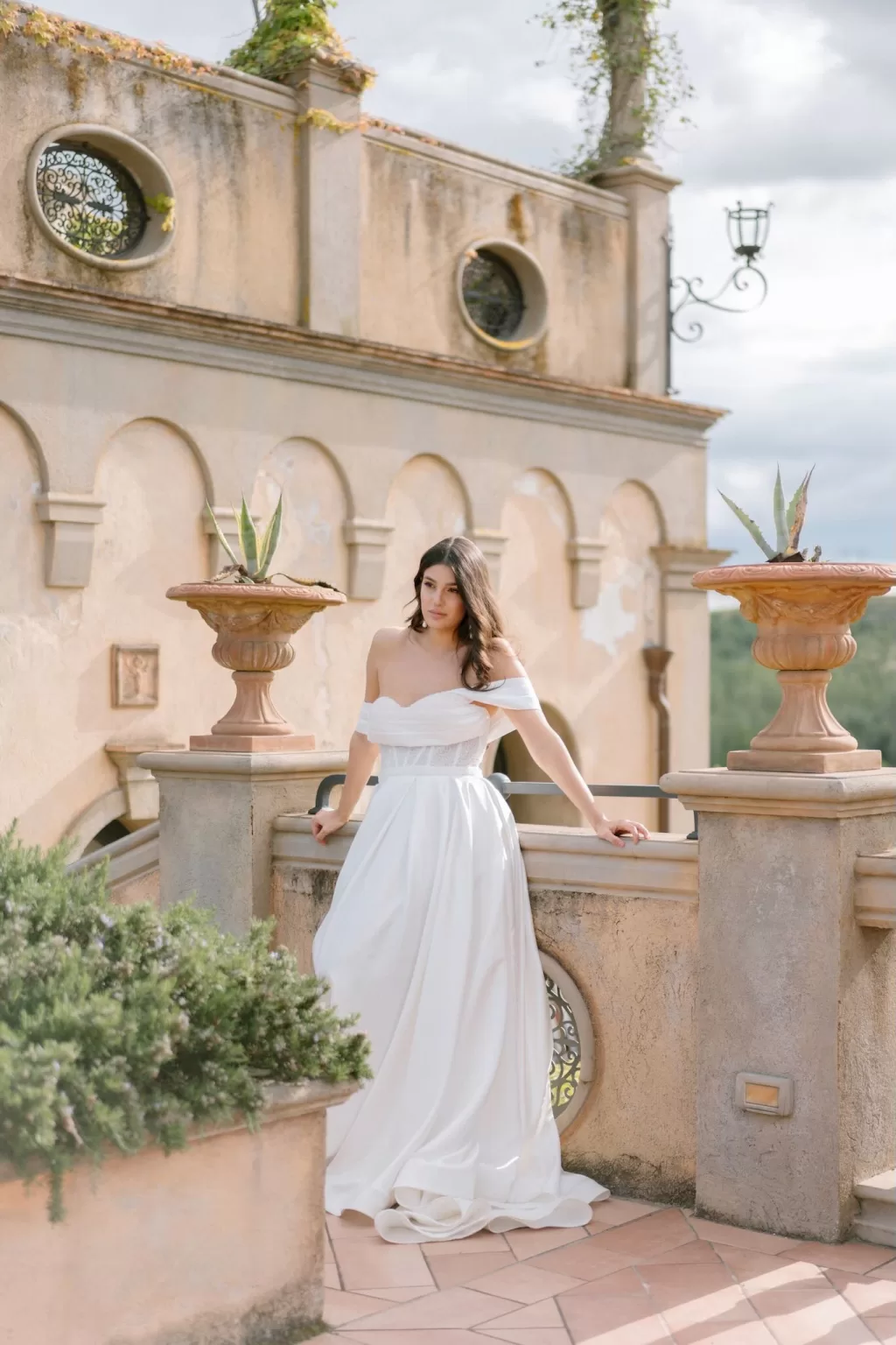Bride posing on the sunlit terrace of Tenuta Corbinaia, surrounded by Tuscan architectural details and potted plants.
