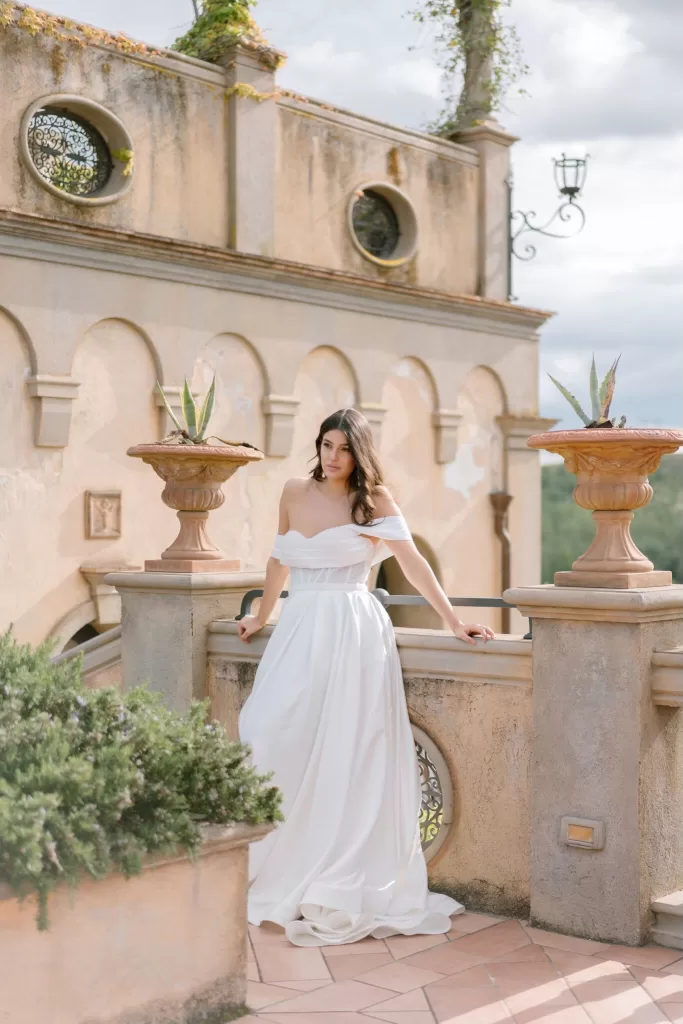 Bride posing on the sunlit terrace of Tenuta Corbinaia, surrounded by Tuscan architectural details and potted plants.