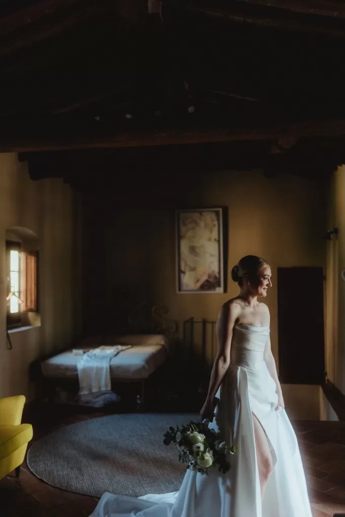 Bride standing with bouquet in a softly lit Castello del Trebbio room before the ceremony.
