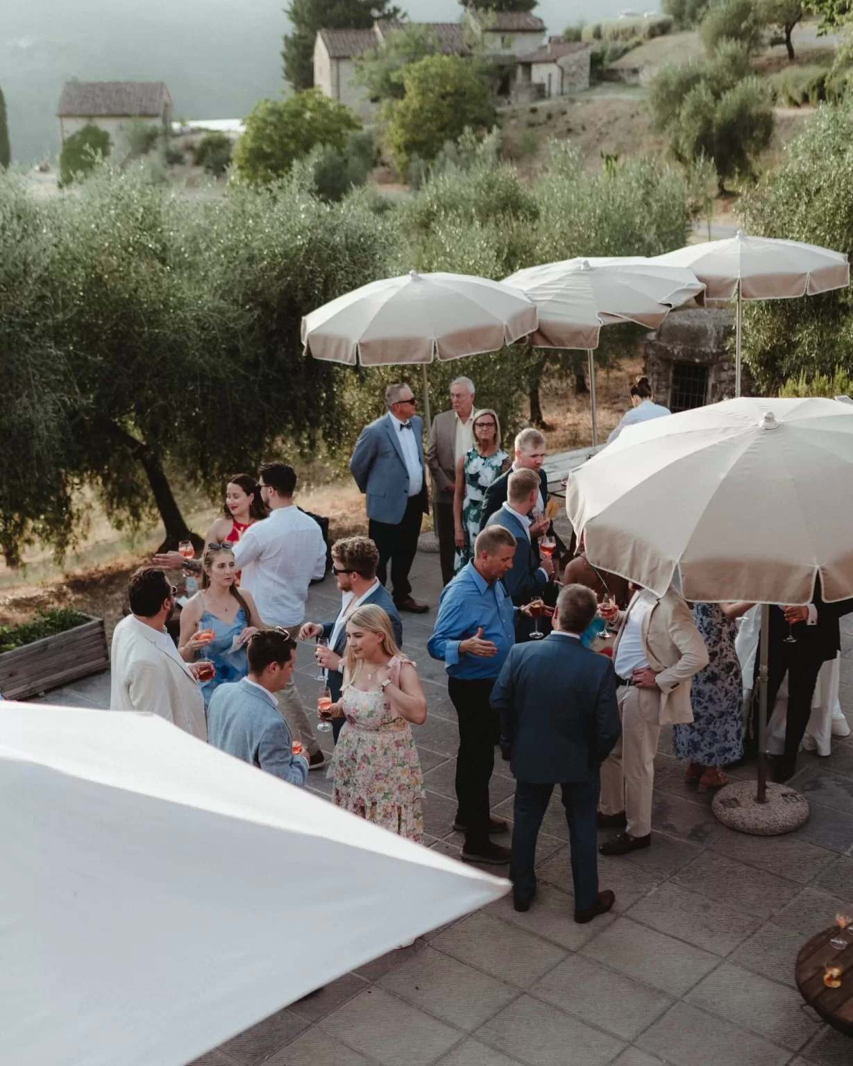 Guests enjoying cocktails under umbrellas at Castello del Trebbio during a summer wedding reception