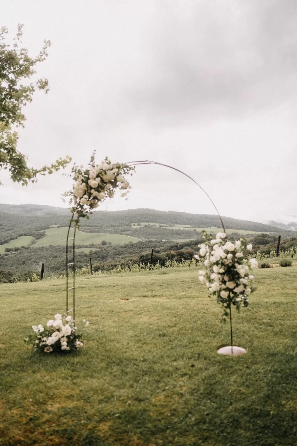 Bride and groom share a kiss under a floral arch on the lush ceremony lawn at Castello di Casole.