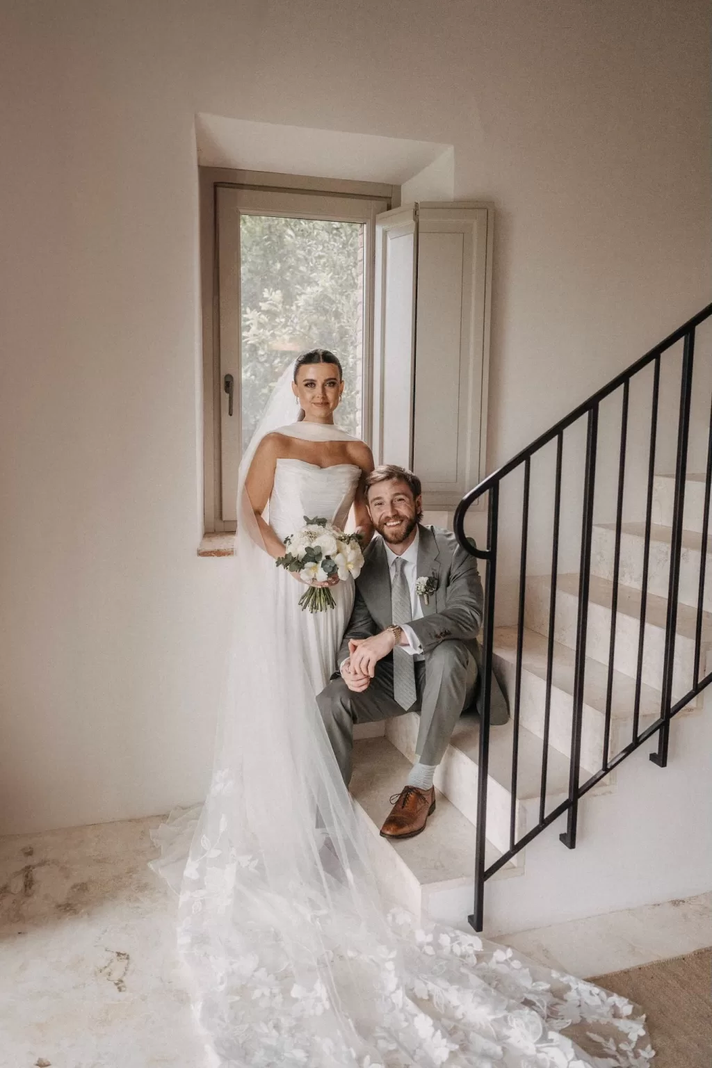 Bride and groom pose together on a stone staircase inside Castello di Casole, bathed in soft natural light.