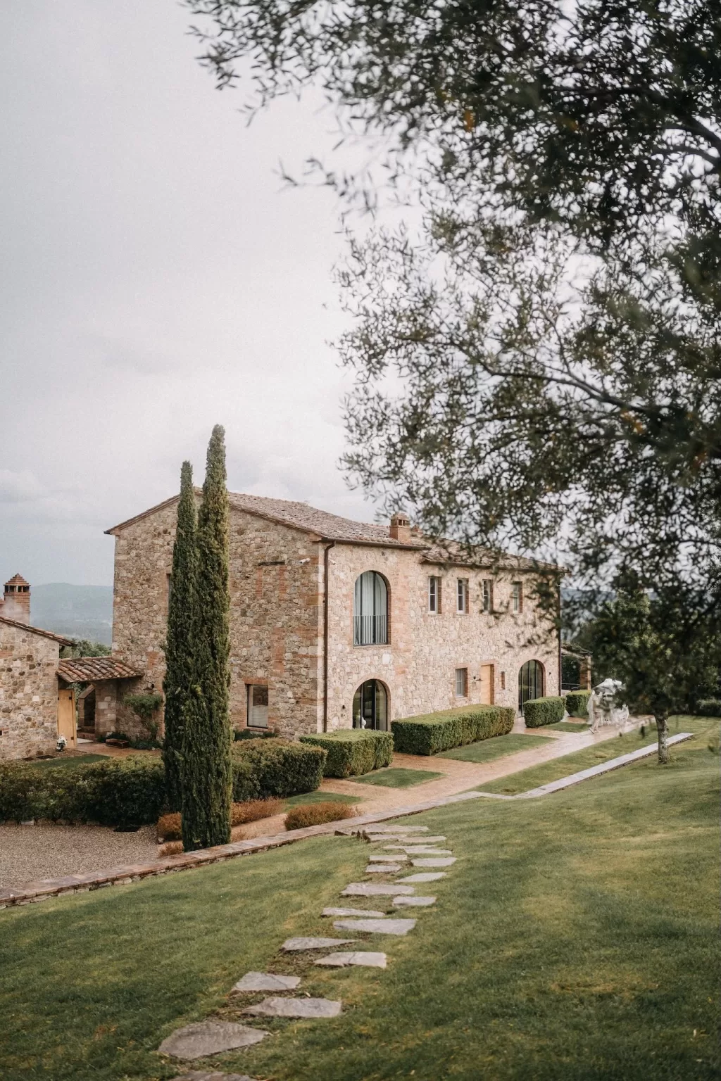 Stone path leading to the sunlit villa at Castello di Casole surrounded by manicured hedges.