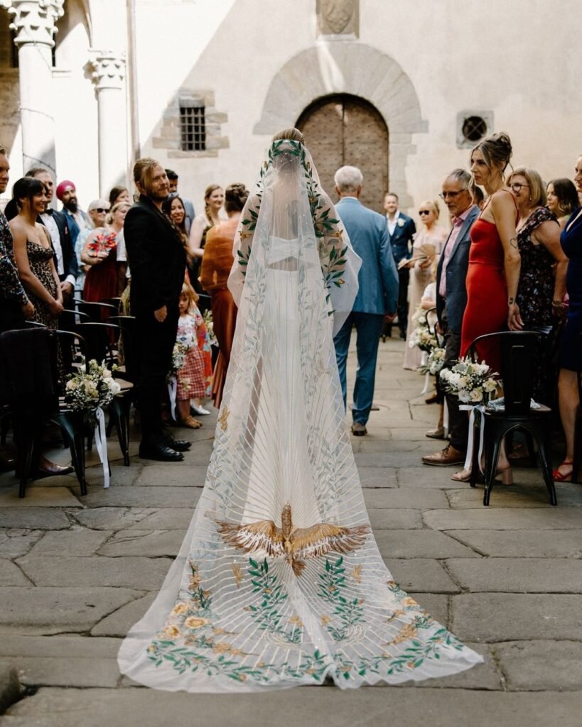 The bride walks down the aisle at Castello del Trebbio, framed by historic stone walls and elegant floral decor, captured by Brandon Scott.