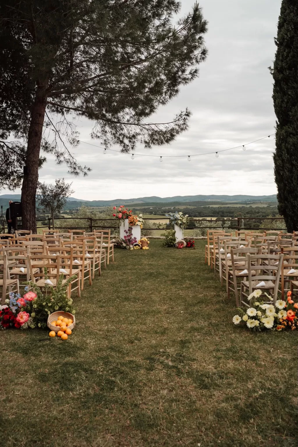 Outdoor ceremony setup with wooden chairs, citrus baskets, and floral pillars overlooking Tuscan hills at Conti di San Bonifacio.