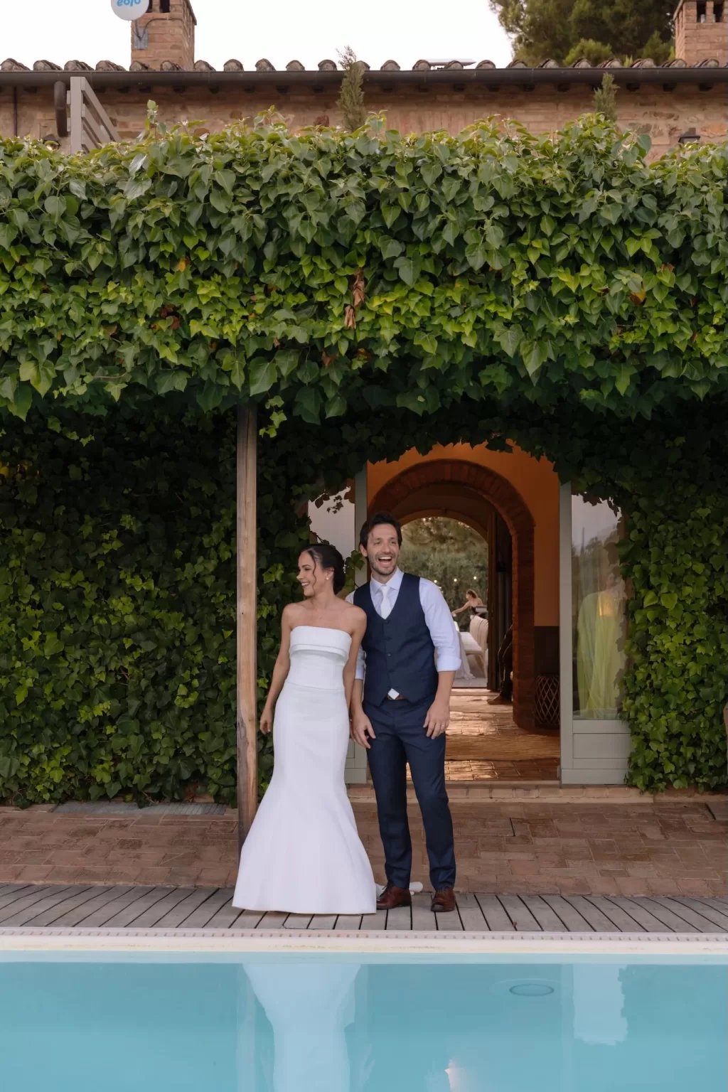 Bride and groom sharing a joyful moment by the ivy-covered villa and pool at Conti di San Bonifacio.