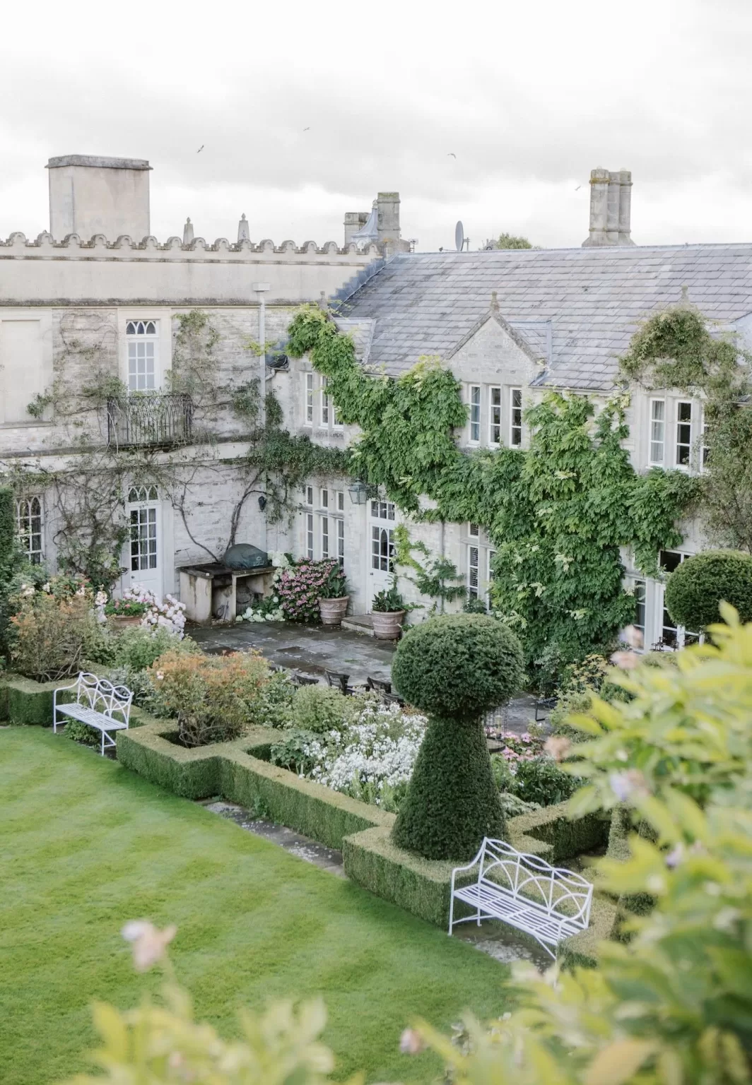 A view across the manicured gardens of Euridge Manor, with climbing vines and shaped topiary against the manor walls.