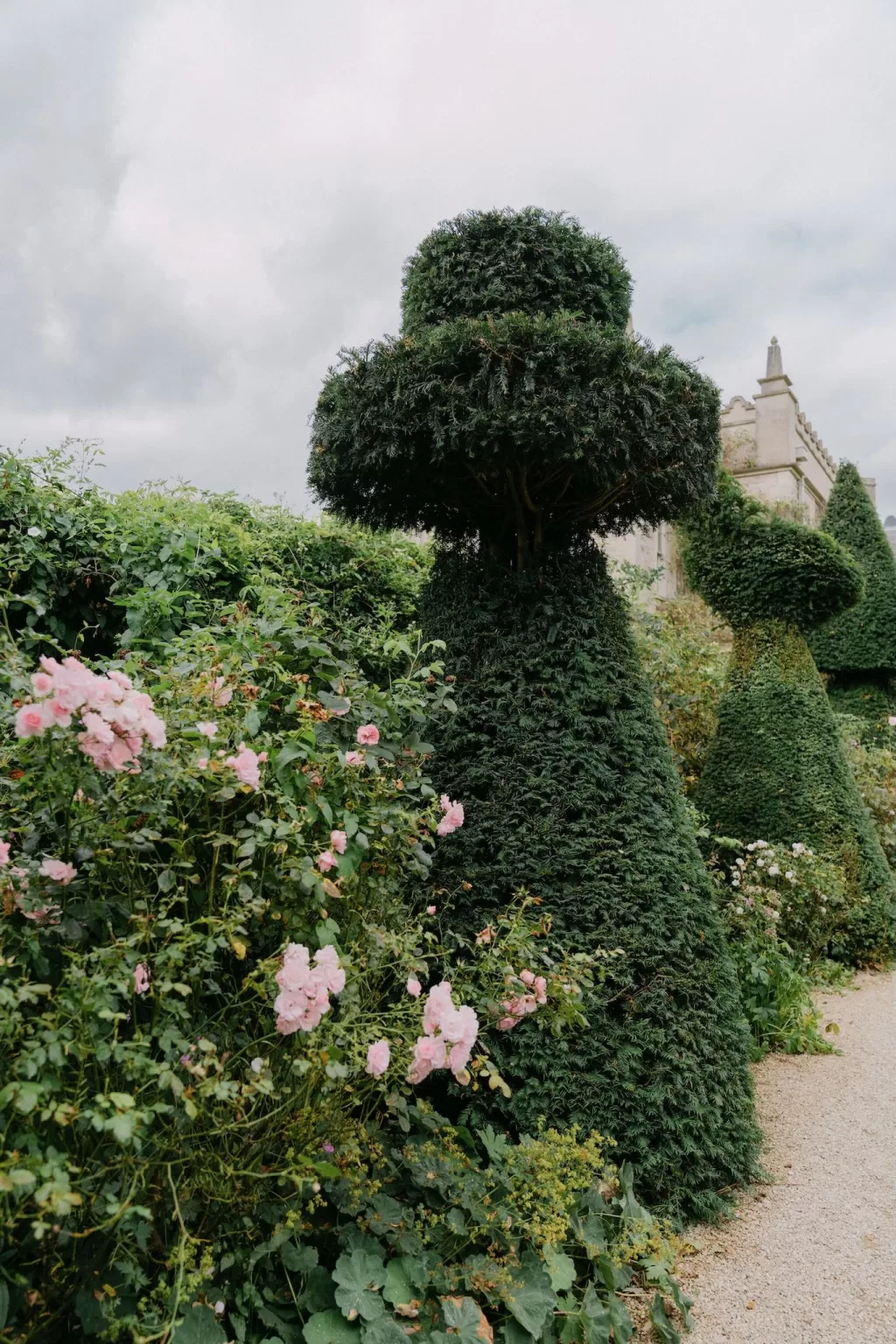 Whimsical topiary trees and pink garden roses line a gravel path at Euridge Manor.