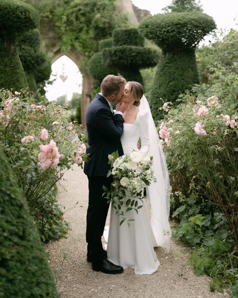The couple shares an intimate moment in the gardens of Euridge Manor, with lush greenery as their backdrop.