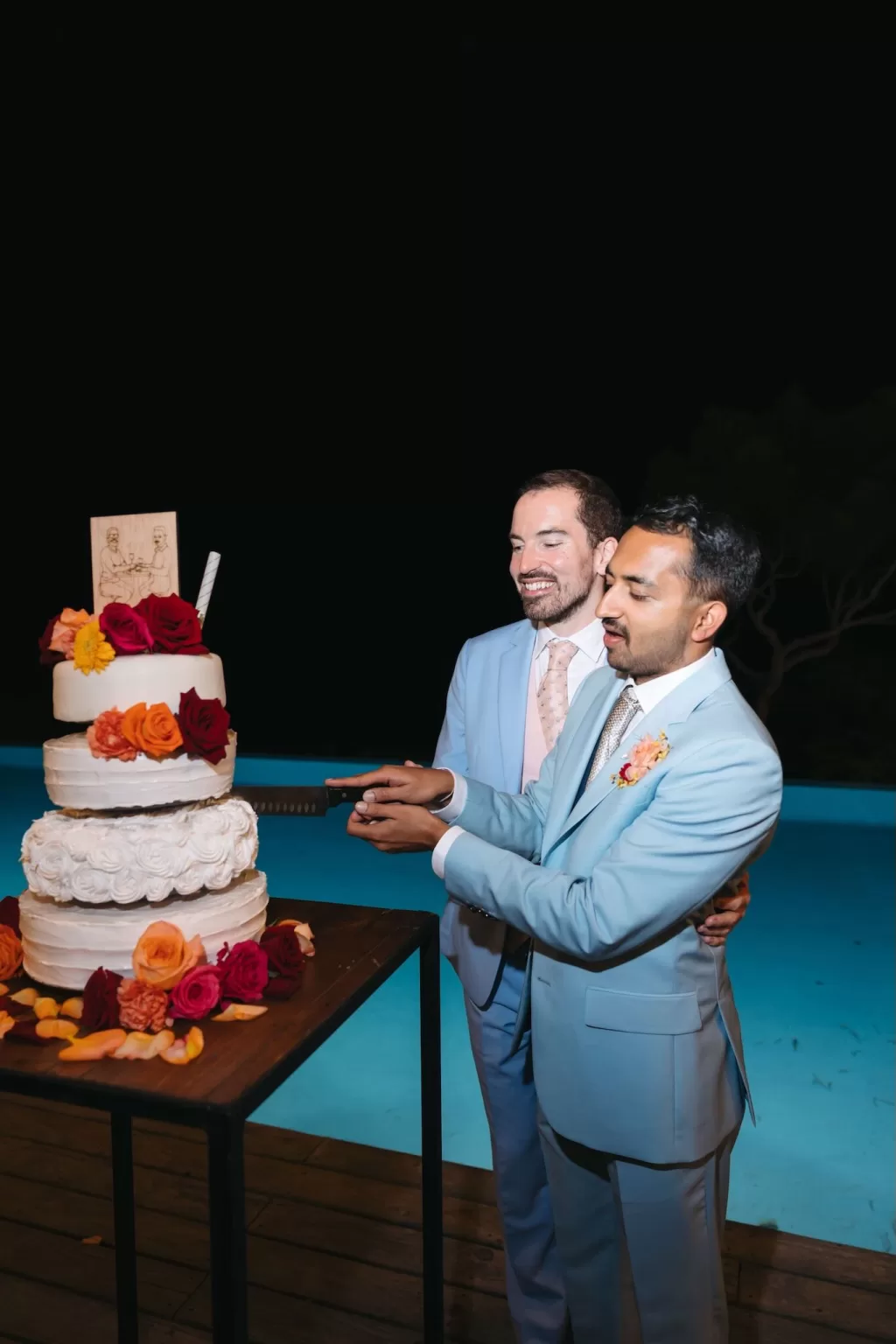 Grooms cutting their wedding cake by the glowing pool at Masia Casa del Mar.