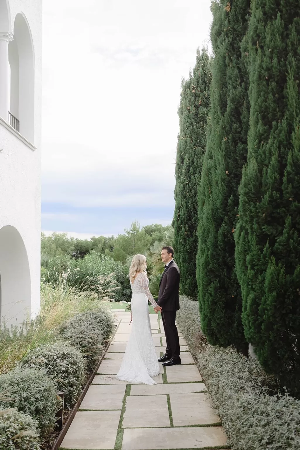 Bride and groom sharing a quiet moment along a manicured garden path at Masia Casa del Mar