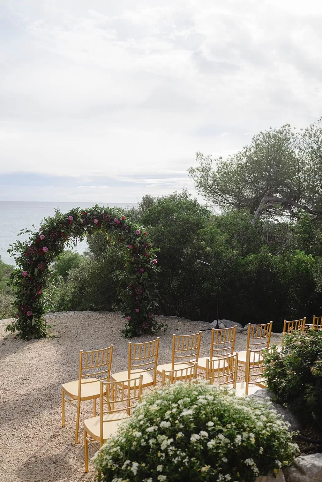 Romantic floral arch framed by golden ceremony chairs and Mediterranean sea backdrop