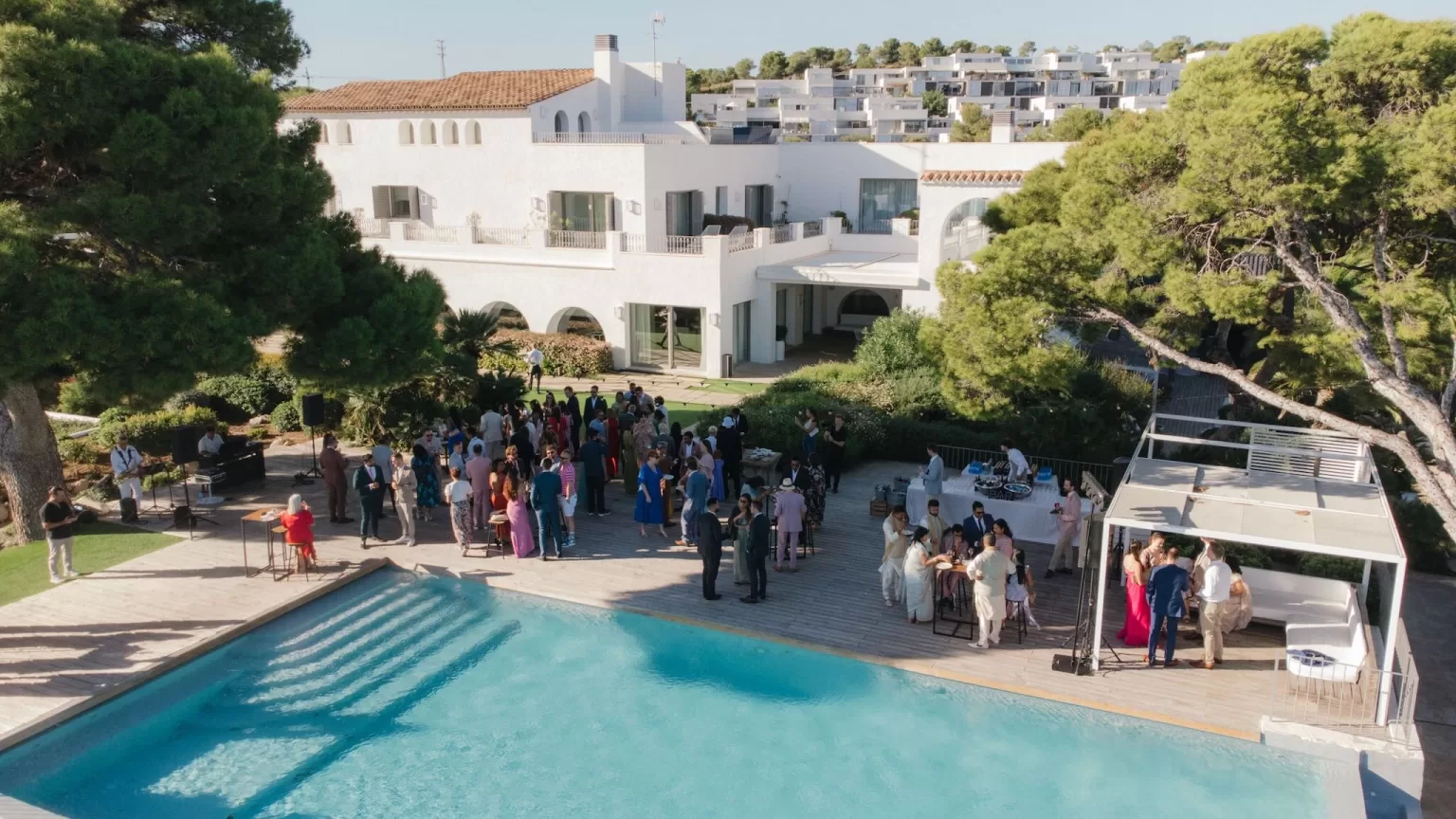 Guests gather by the poolside for a lively cocktail reception at Masia Casa del Mar, surrounded by whitewashed architecture and sea views.