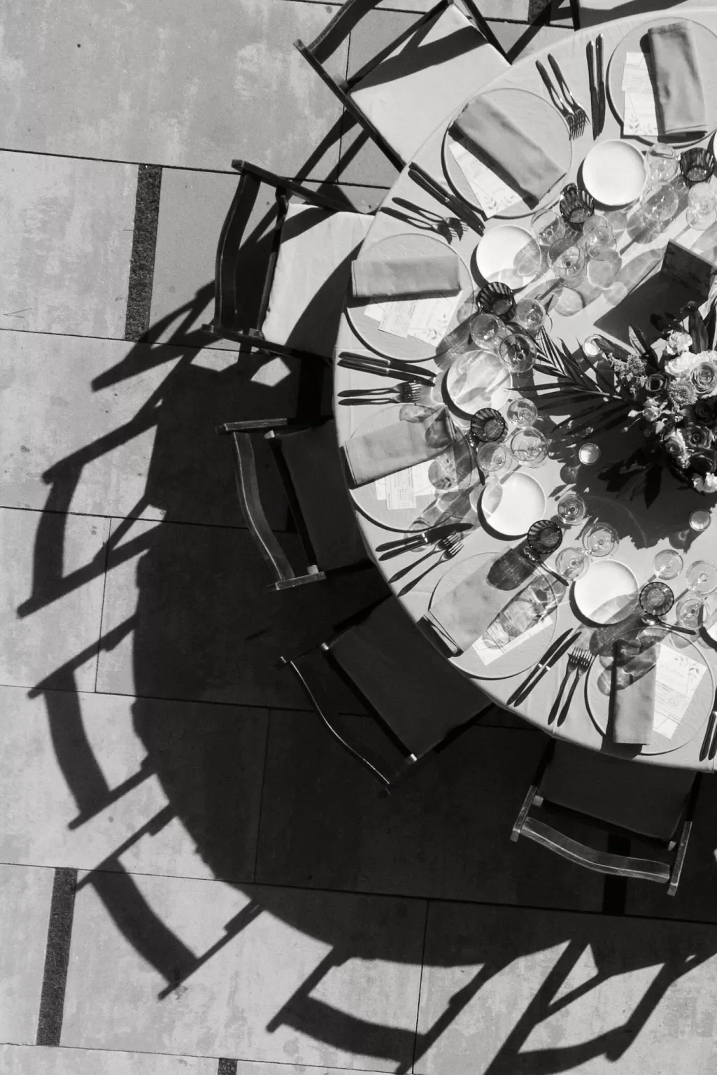 Dramatic black and white image of a reception table casting crisp shadows on the stone terrace at Masia Casa del Mar.