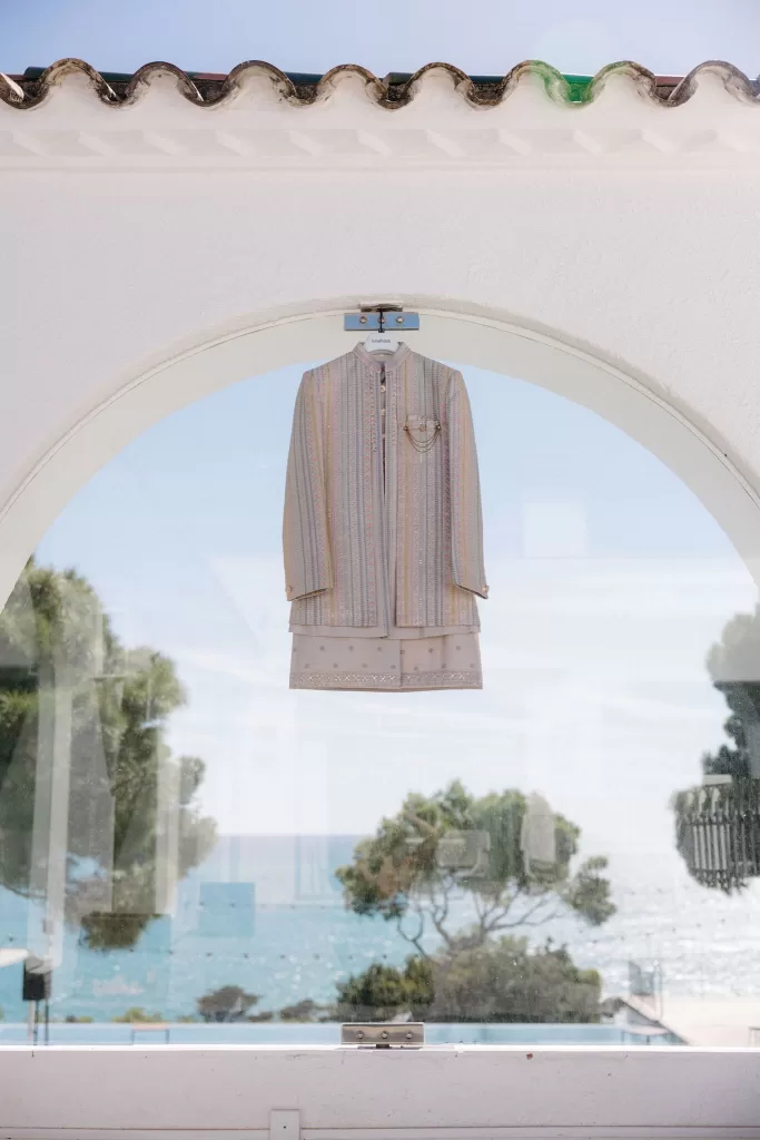 Pastel striped sherwani and embroidered kurta hung by an arched window overlooking the Mediterranean at Masia Casa del Mar.