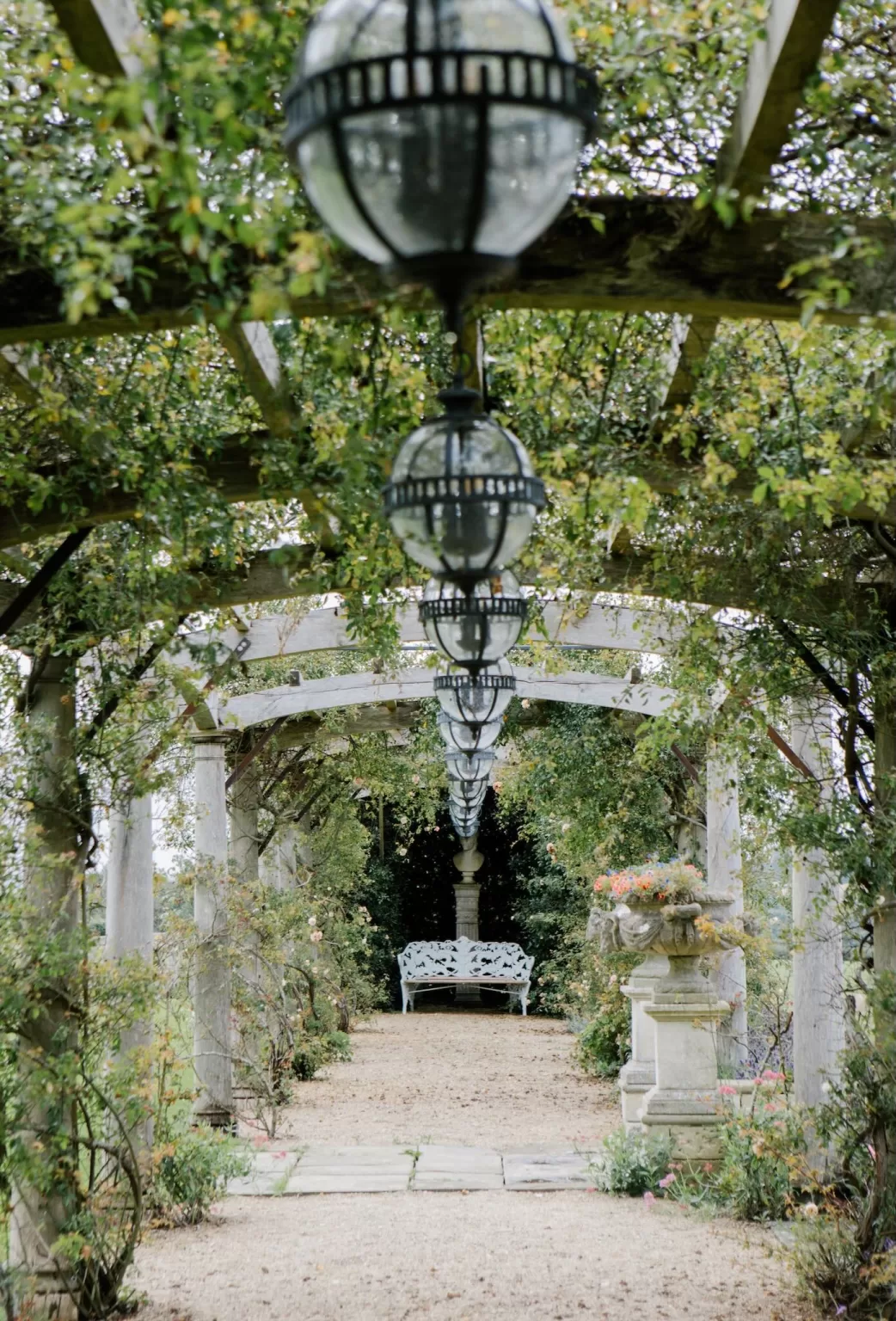A romantic garden pergola at Euridge Manor with vintage hanging lanterns and a bench at the end of the path.