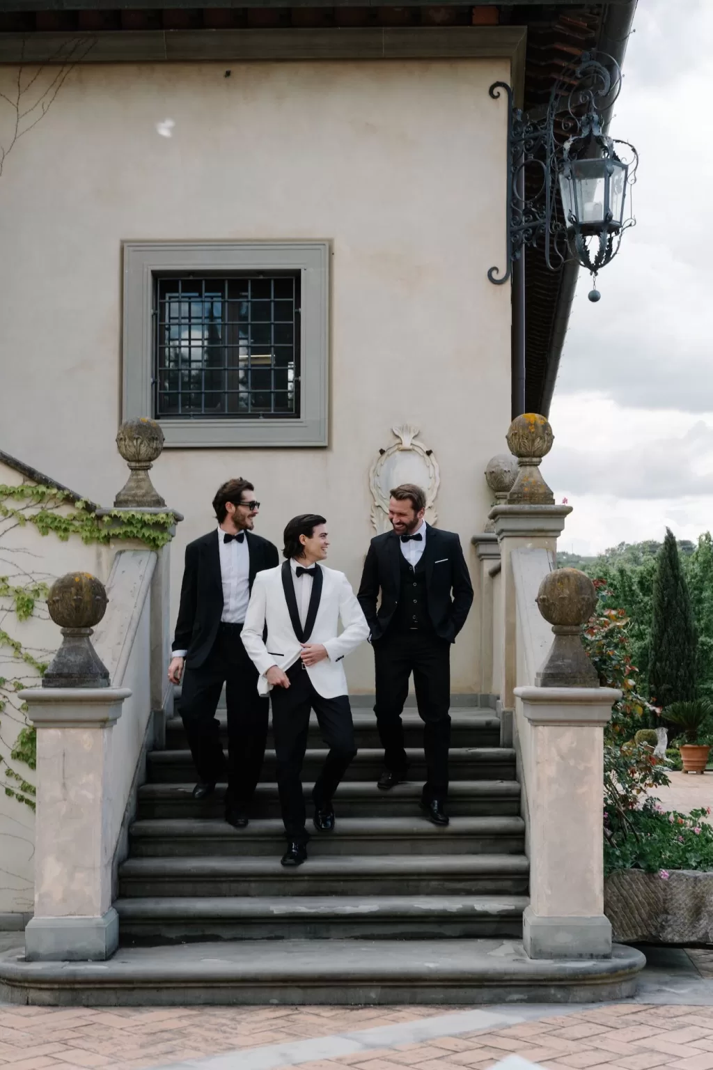 Groom and groomsmen in classic tuxedos sharing a lighthearted moment on the villa steps at Tenuta Corbinaia.
