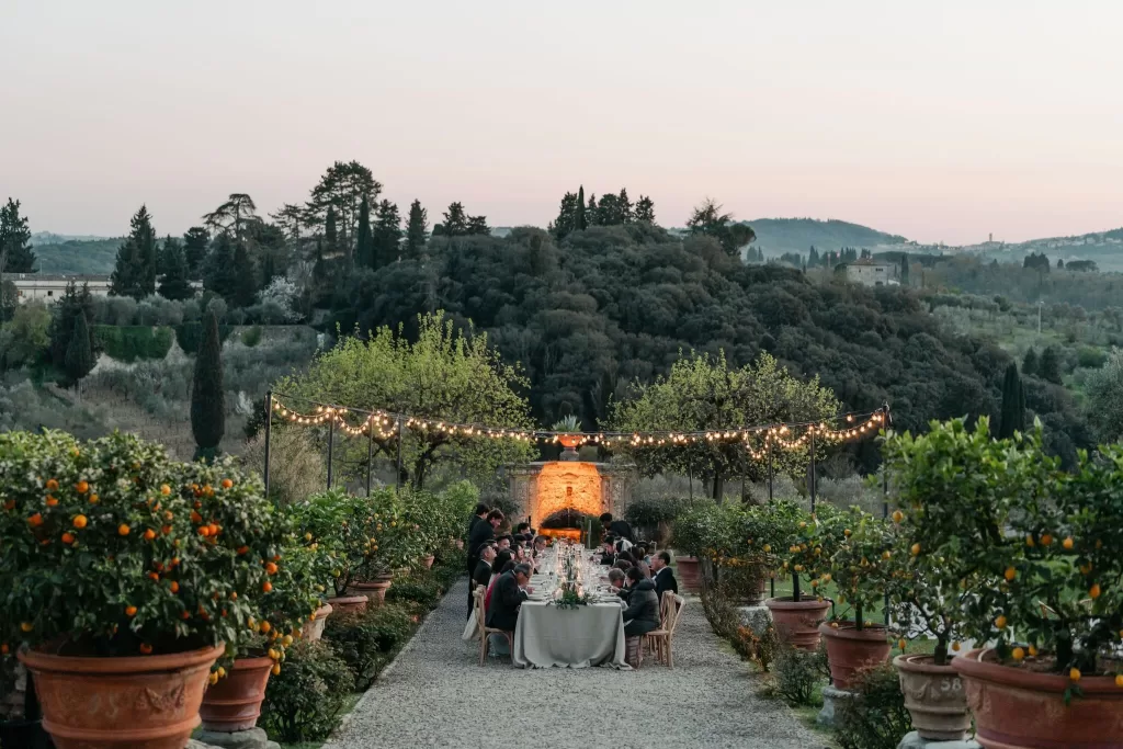 Guests dining under glowing string lights at sunset in the lemon grove of Villa Medicea di Lilliano.