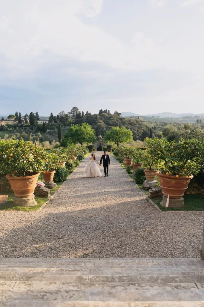 Bride and groom walking hand in hand through the lemon garden at Villa Medicea di Lilliano with rolling hills behind them.