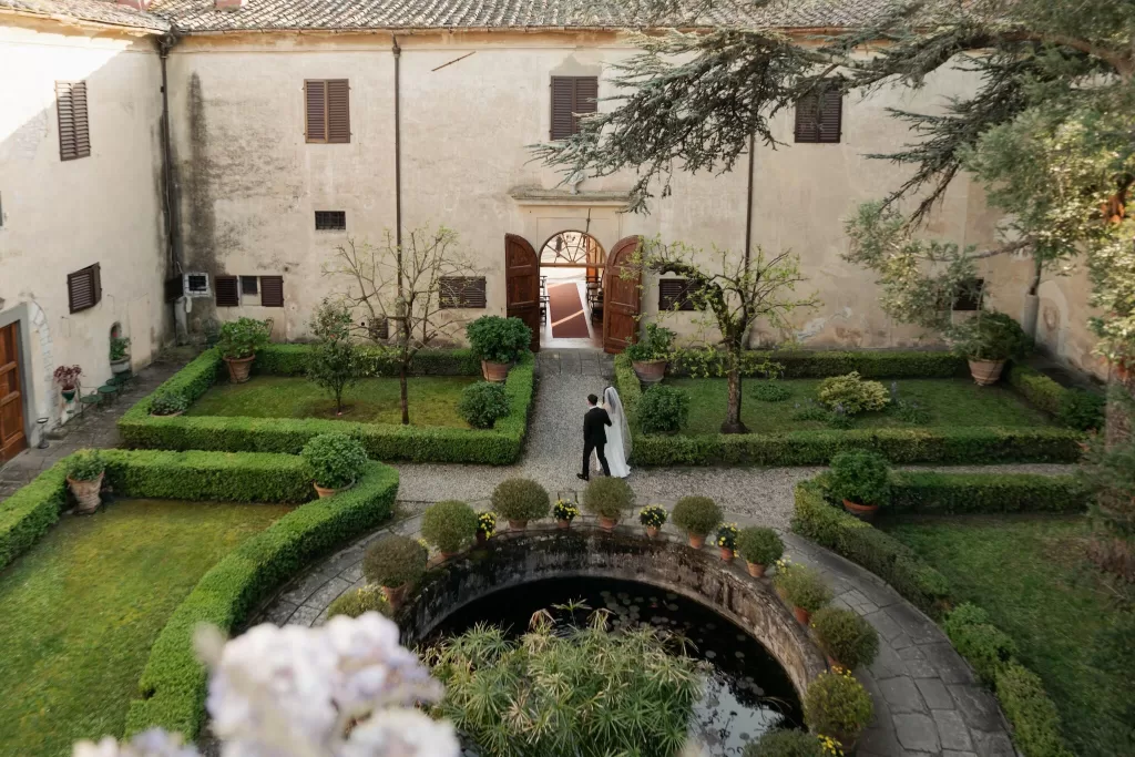 Bride and groom strolling through the courtyard garden of Villa di Maiano toward the villa.