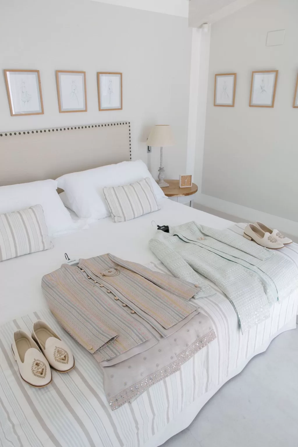 Two grooms' wedding outfits laid out on a striped bedspread in a calm, coastal room at Masia Casa del Mar.