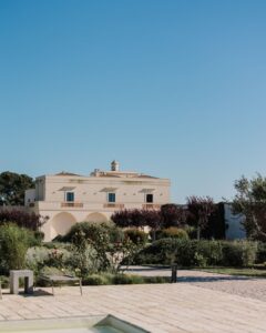 Grand entrance to Masseria Fontana di Vite, framed by lush greenery and bathed in warm Mediterranean sunlight.