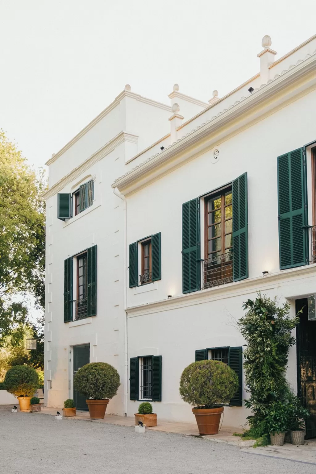 Elegant side view of Masia Aldamar’s white facade with green shutters and potted trees