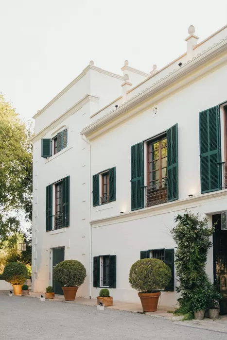 Elegant side view of Masia Aldamar’s white facade with green shutters and potted trees