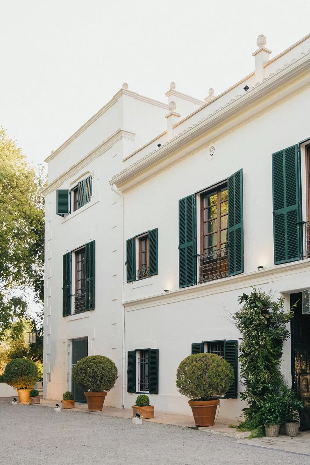 Elegant side view of Masia Aldamar’s white facade with green shutters and potted trees