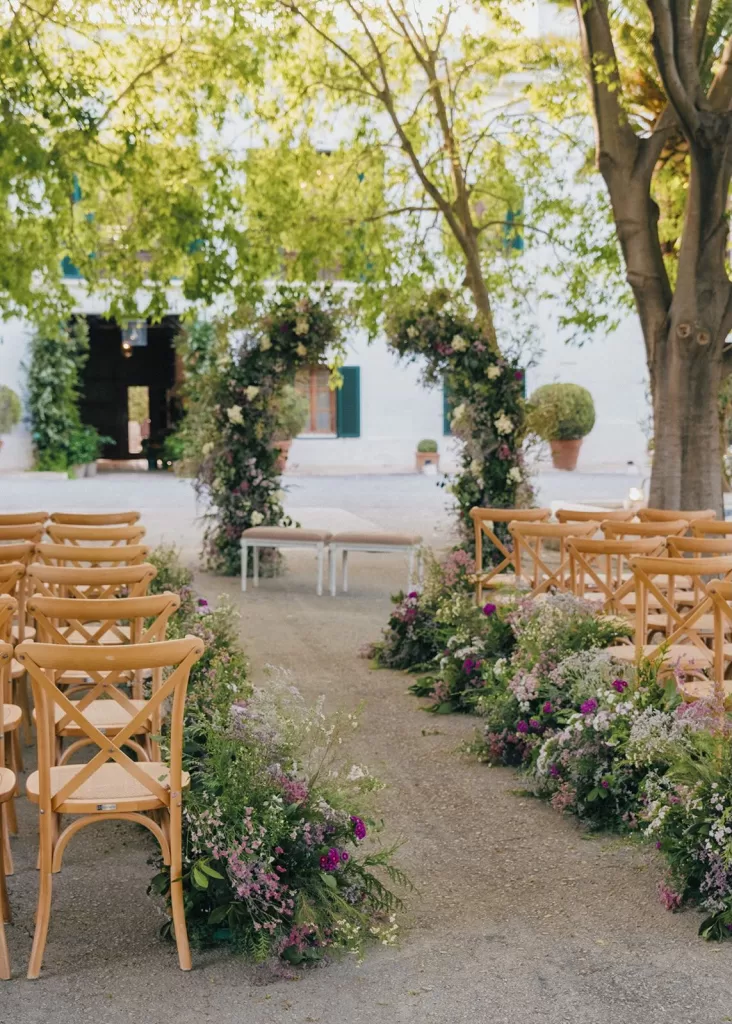 Flower-lined wedding ceremony aisle with wooden chairs at Masia Aldamar