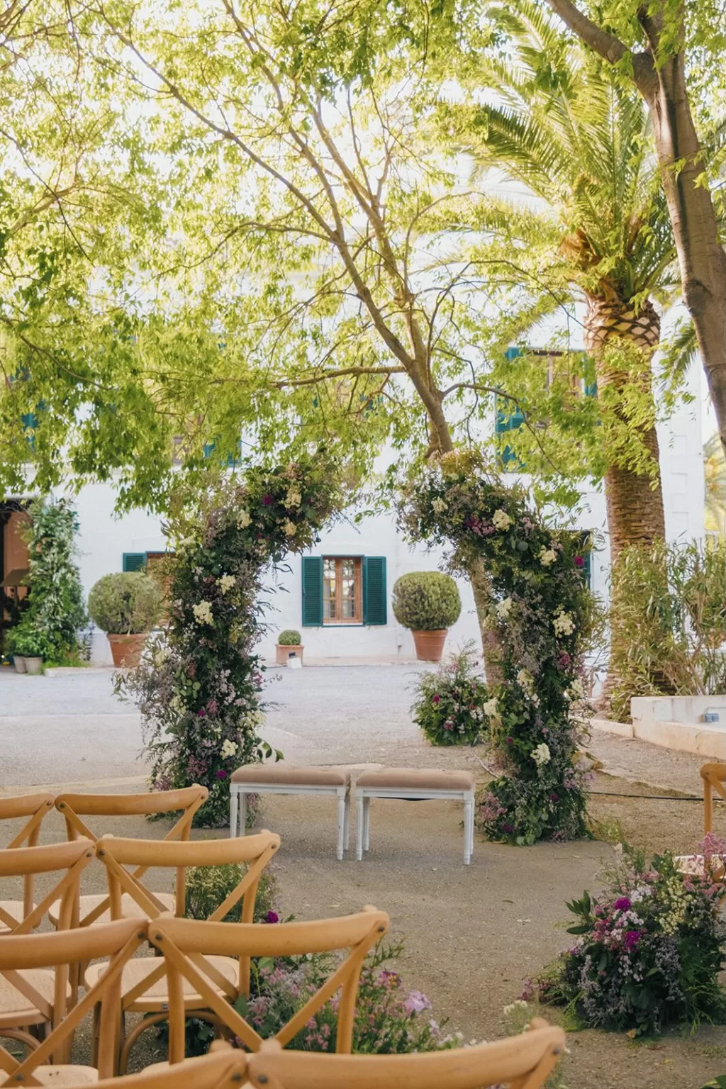 Floral wedding ceremony arches under green trees at Masia Aldamar
