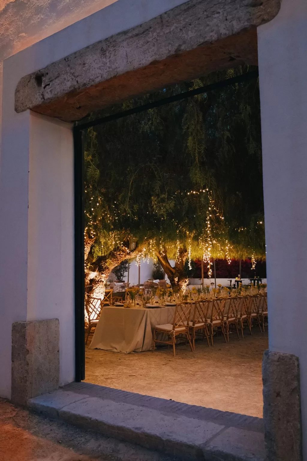 Magical outdoor wedding dinner under fairy lights at Masia Aldamar seen through stone doorway