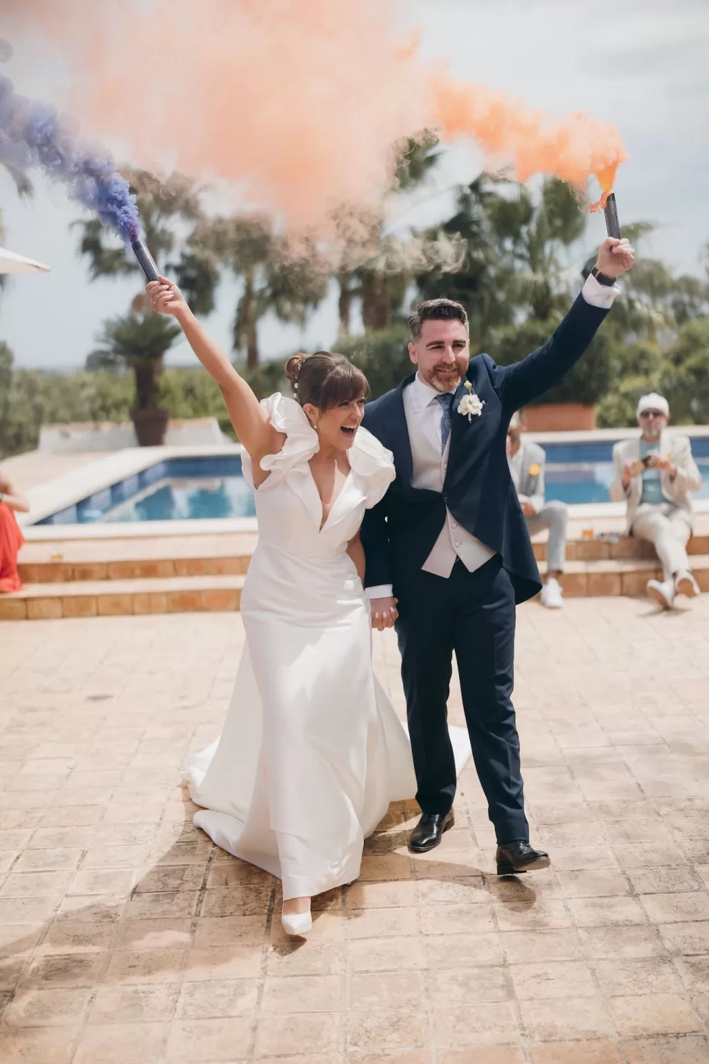 Bride and groom celebrate with colorful smoke flares by the poolside at Masia Aldamar.