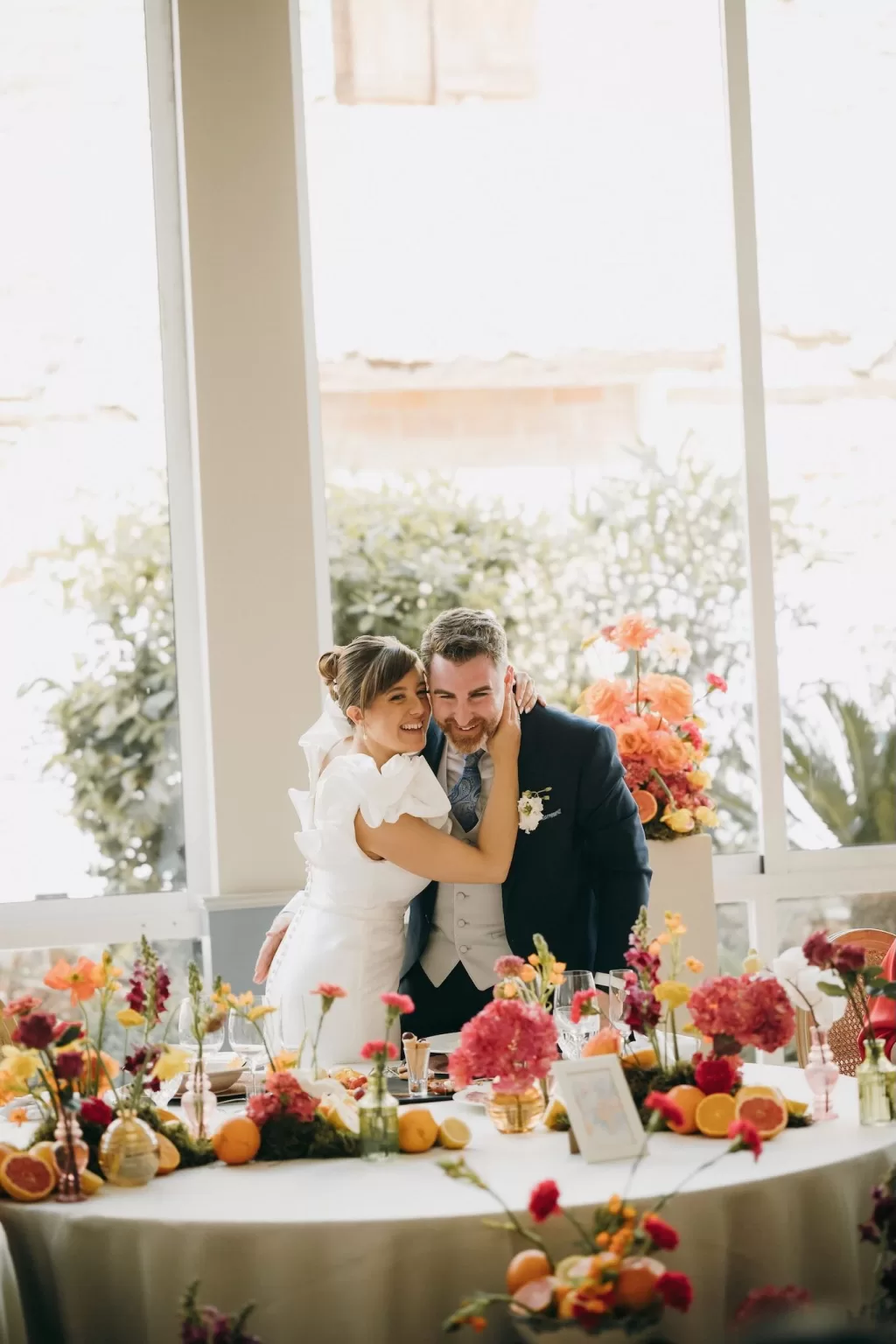 Bride embracing groom at a flower-filled reception table in Masia Aldamar.