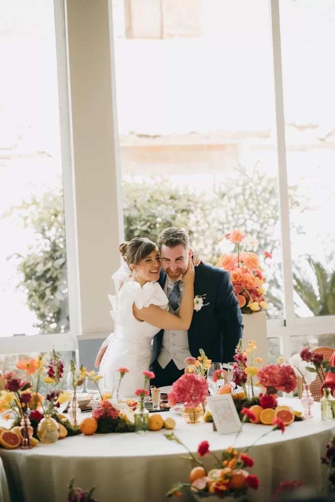 Bride embracing groom at a flower-filled reception table in Masia Aldamar.