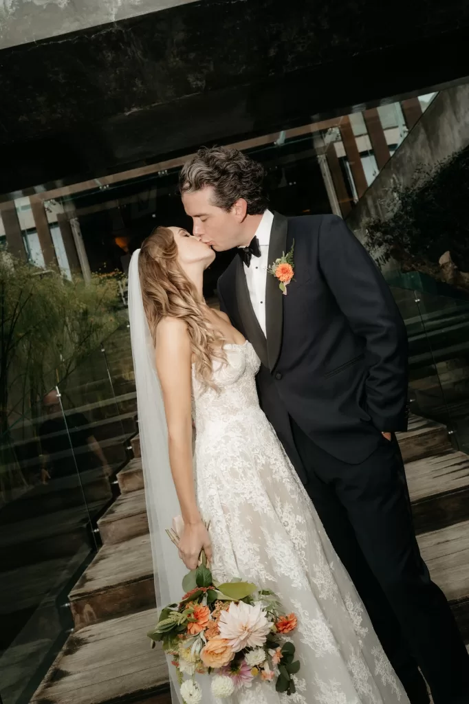 Bride and groom kissing beside the modern glass and concrete architecture at Areias do Seixo.