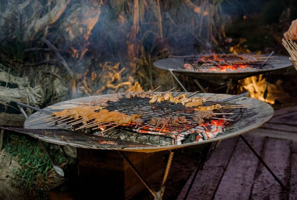 An open grill at Areias do Seixo, where flames rise as chefs prepare a feast for the wedding reception.
