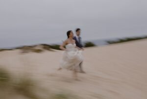 Barefoot on the sand, the couple walks hand in hand as gentle waves lap at their feet.