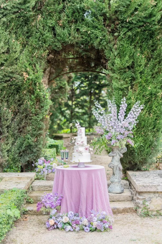 Cake table set in the lush Bastide du Roy garden with candles, wildflower garlands, and elegant linens for a whimsical dessert experience.