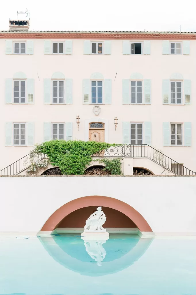 View of the reflective pool and classical statue at Bastide du Roy, framed by manicured hedges and stone pergolas at sunset.