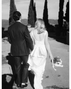 The couple walks hand in hand towards the iconic cypress tree-lined path at Rosewood Castiglion del Bosco, bathed in golden light.