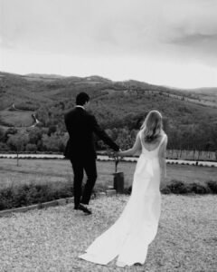 The couple walks hand in hand through the scenic grounds of Rosewood Castiglion del Bosco, surrounded by Tuscan landscapes.