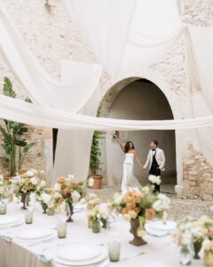 Joyful bride and groom entering hand-in-hand, celebrating in the beautifully decorated courtyard of Finca Morneta.